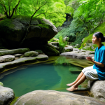A person, fully clothed in comfortable, modest wellness attire, sits peacefully on a smooth rock beside a natural hot spring. Gentle steam rises from the warm, mineral-rich water, surrounded by lush green foliage and ancient rock formations. Soft, diffused natural light illuminates the scene, creating a serene and introspective atmosphere. The person's posture is calm and natural, reflecting deep relaxation and a digital detox experience. Perfect anatomy, correct proportions, natural pose, well-formed hands, proper finger count, natural body proportions. Safe for work, appropriate content, fully clothed, modest, family-friendly.